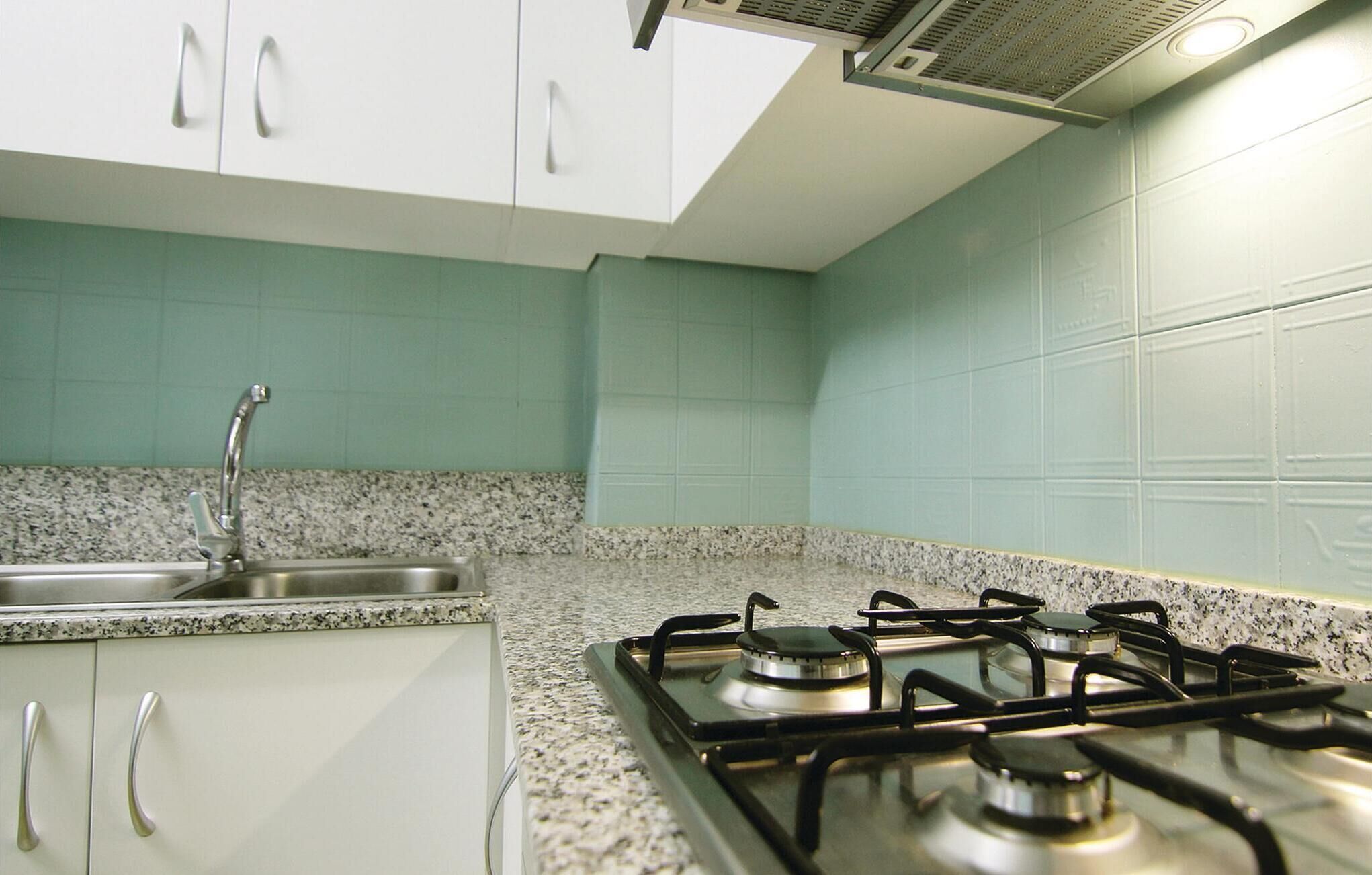 Une cuisine avec des meubles blancs, un plan de travail en granit, un évier en acier inoxydable et une cuisinière à gaz.