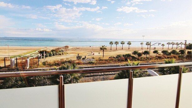 Vista costera con playa, palmeras y una vía de tren.