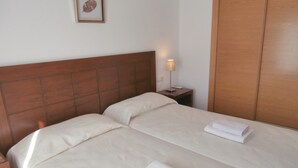 Un lit bien fait, avec une tête de lit en bois, une lampe de chevet et une serviette pliée posée sur la table de chevet.