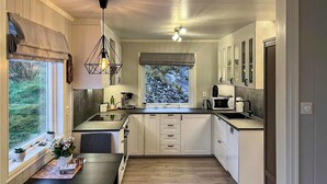 A compact kitchen with white cabinets, a dining table, and a window with a view of greenery. - Amazing home in Etne with WiFi (Etne)