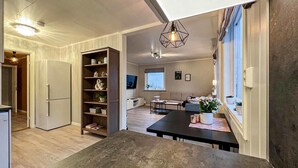 A modern kitchen with a built-in refrigerator, a wooden shelving unit, and a dining area with a dark table. - Amazing home in Etne with WiFi (Etne)
