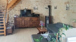Un salon rustique avec un mur en pierre, un escalier en bois, une télévision, une cheminée et un canapé.