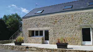 Un bâtiment en pierre avec un toit en pente, une petite entrée et deux plantes en pot sur le porche.