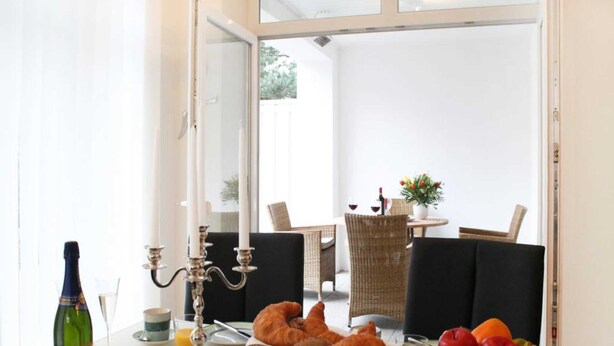 A breakfast setup with croissants, fruit, and juice on a table, with a bottle of wine and a candelabra in the foreground. - At the Dünenweg uns Hüsung Whg. 3 - at the dune path uns Hüsung Whg. 3 (Ostseebad Boltenhagen)