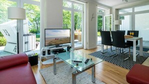A modern living room with a glass coffee table, a flat-screen TV, and a dining area with black chairs and a table. - At the Dünenweg uns Hüsung Whg. 3 - at the dune path uns Hüsung Whg. 3 (Ostseebad Boltenhagen)