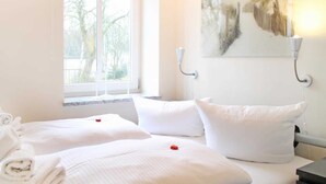 A hotel room with two beds, a window with a view of trees, and a painting on the wall. - At the Dünenweg uns Hüsung Whg. 3 - at the dune path uns Hüsung Whg. 3 (Ostseebad Boltenhagen)