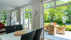 A modern living room with a dining area, large windows, and a view of a garden. - At the Dünenweg uns Hüsung Whg. 3 - at the dune path uns Hüsung Whg. 3 (Ostseebad Boltenhagen)