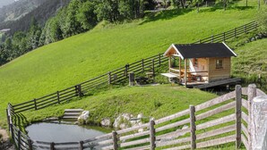 A wooden cabin with a deck, surrounded by a wooden fence, and a small pond in the foreground. - sehr schoene Ferienwohnung (Schladming)