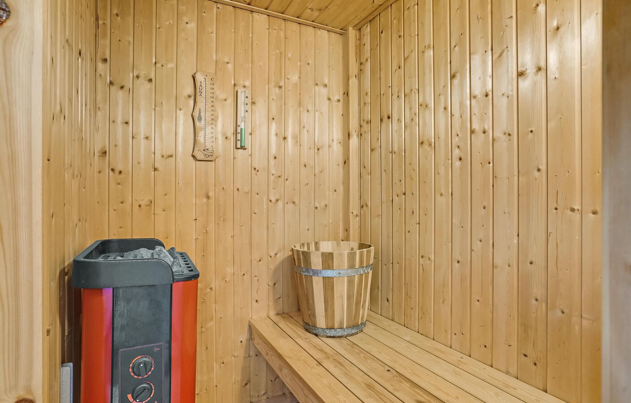 A sauna room with wooden walls, a bench, a sauna heater, and a wooden bucket.
