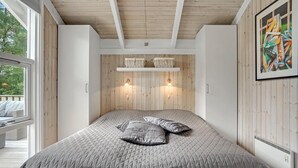 A bedroom with a large bed, wooden ceiling, two wall-mounted lamps, and a window with a view of trees. - 3 bedroom stunning home in Glesborg (Glesborg)