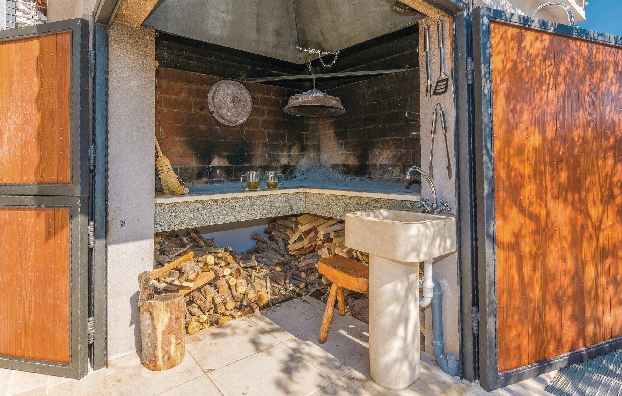 Una cocina rústica al aire libre con chimenea de ladrillo, un colgador para ollas y un lavamanos.