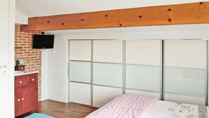Ein Schlafzimmer mit Holzboden, einem roten Schrank, einem an einer Ziegelwand befestigten Fernseher und einem Schiebeglastüren-Kleiderschrank.