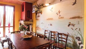 Un espace repas agrémenté d’une fresque représentant des oiseaux et de l’eau, d’une cheminée et de meubles en bois.