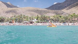 Una playa con agua turquesa cristalina, palmeras y montañas al fondo.