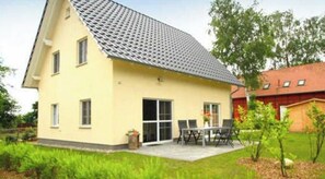 Een twee verdiepingen tellend huis met een pannendak, een terras met tuinmeubilair en een kleine tuin.