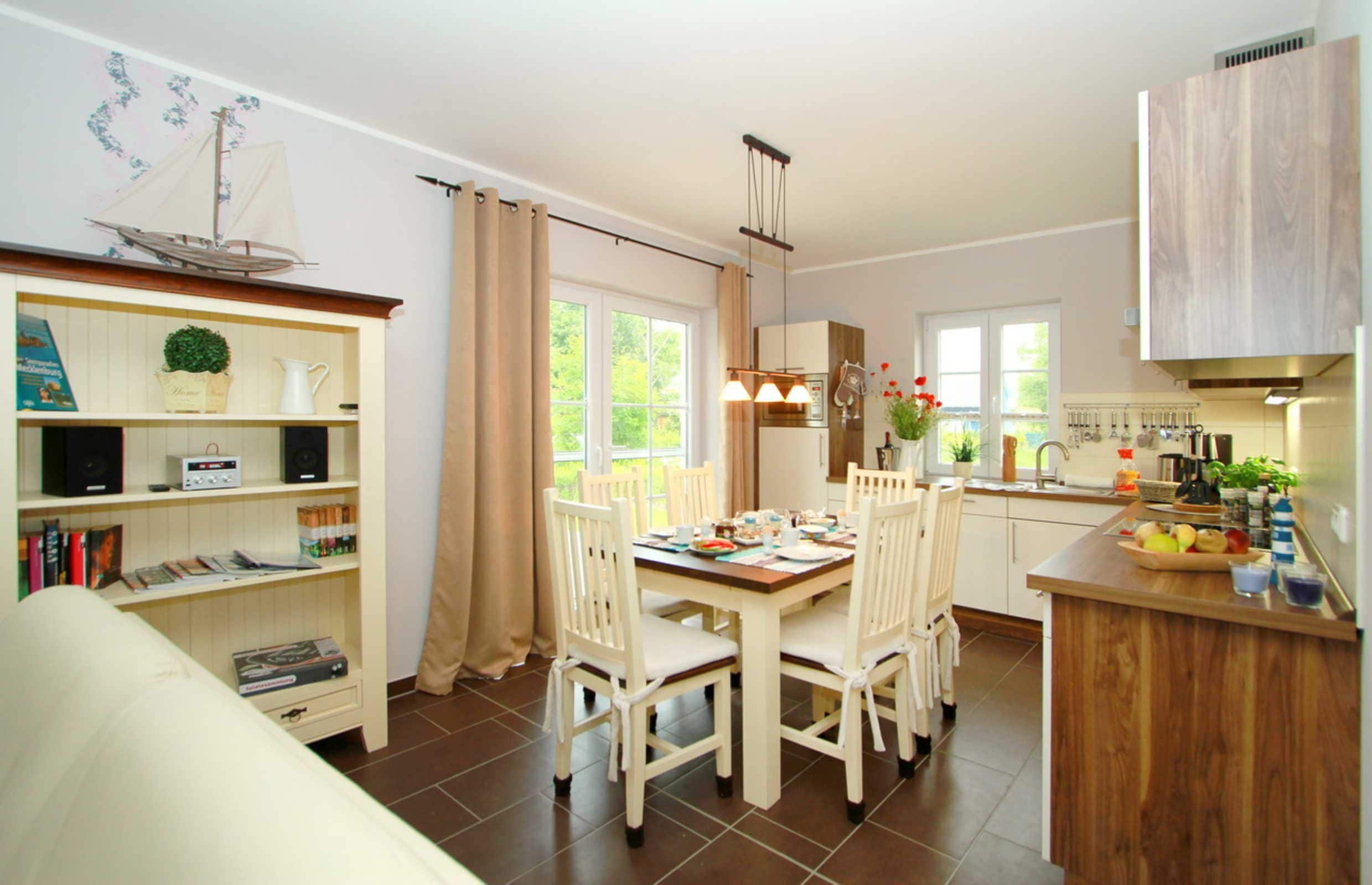 A dining area with a table and chairs, a kitchen with cabinets and a sink, and a bookshelf with various items.