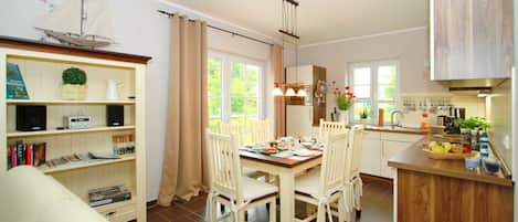 A dining area with a table and chairs, a kitchen with cabinets and a sink, and a bookshelf with various items.