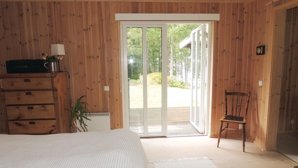 Une chambre à coucher comprenant un lit, une commode, une chaise et une porte-fenêtre coulissante donnant sur une terrasse.