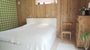 Une chambre à coucher avec un lit doté d’une tête de lit en bois, une table de chevet en bois, une chaise, une commode et une petite fenêtre.