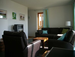 A living room with a sofa, a chair, a small table, a television, and a window with curtains.