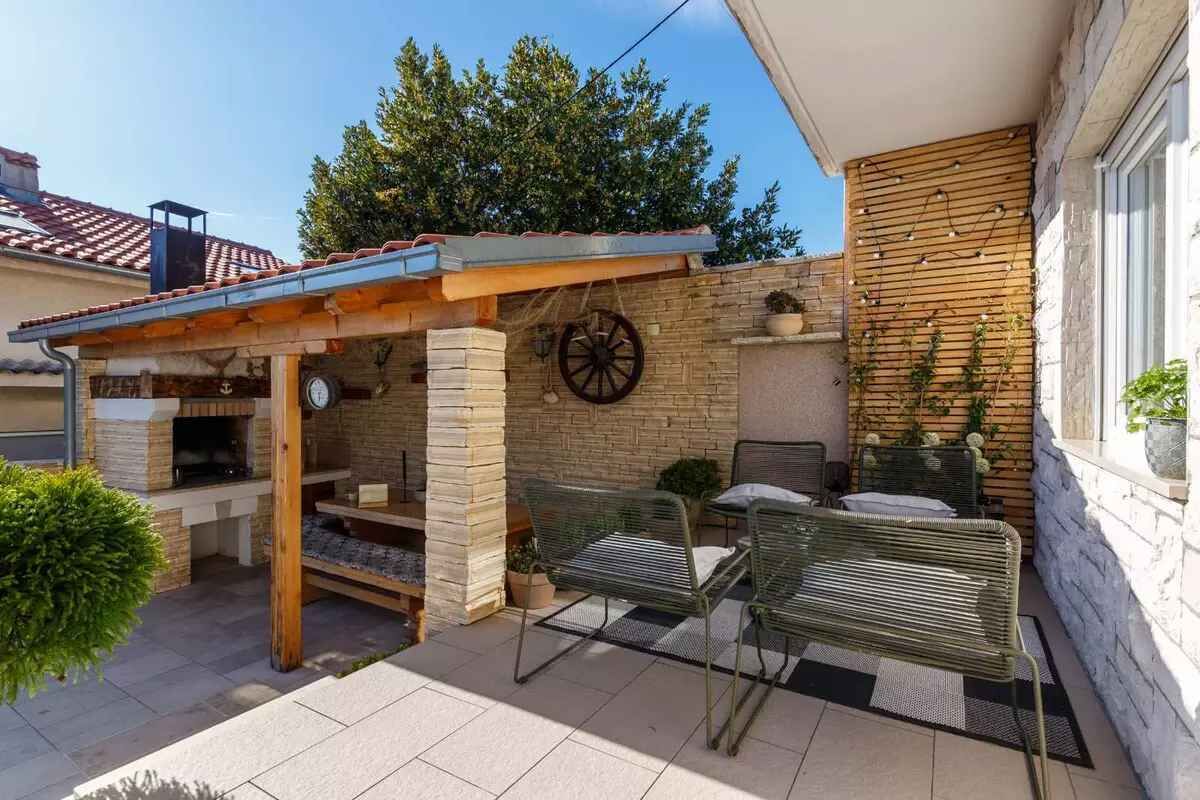A patio area with a pergola, outdoor seating, a stone wall, and a brick fireplace.