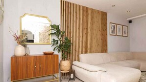 Ein Wohnzimmer mit einem beigefarbenen Sofa, einem Holzkabinett, einem großen Spiegel und einer vertikalen Holzwand.