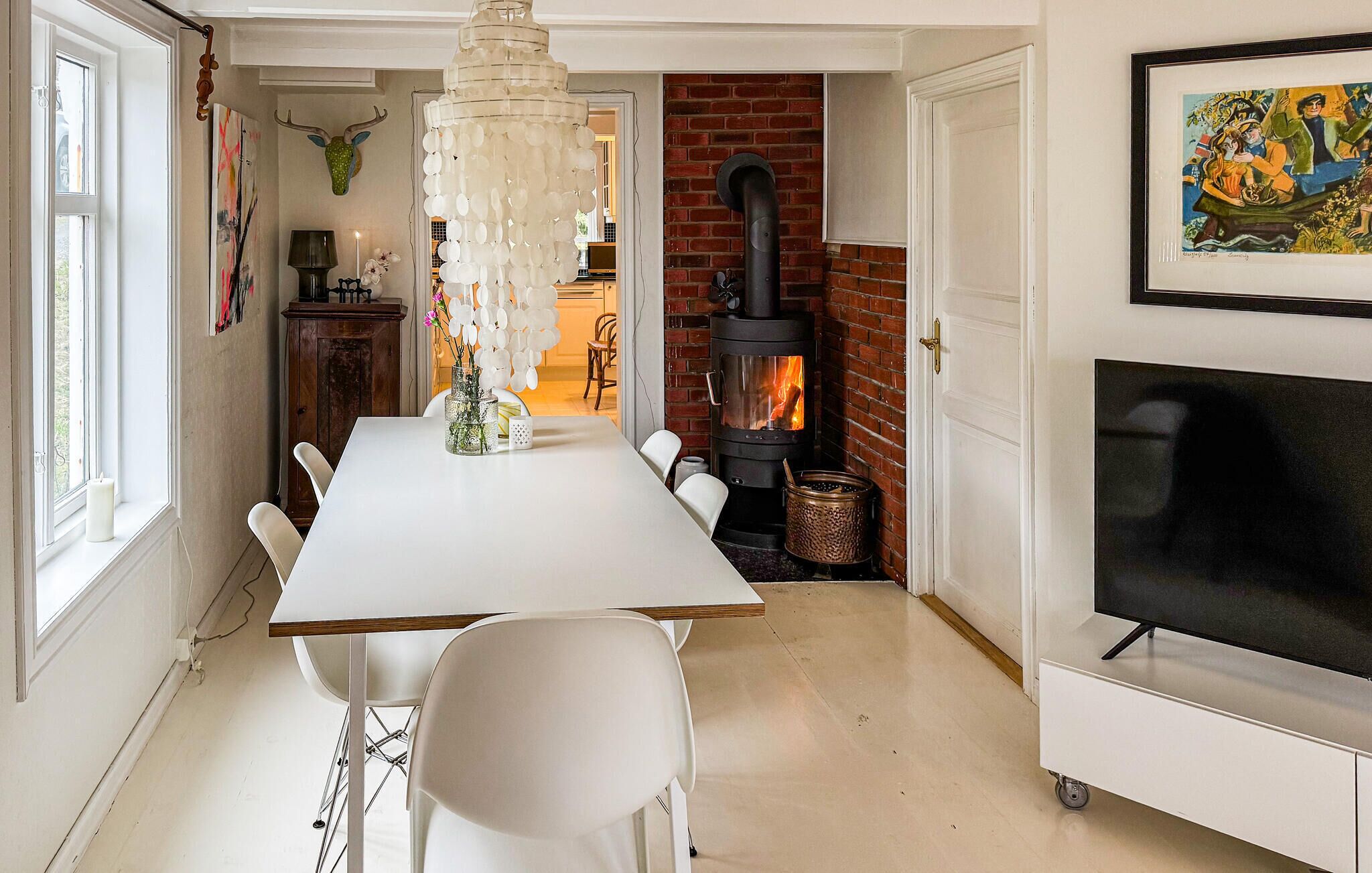 A dining area with a white table, chairs, a chandelier, a fireplace, and a TV.