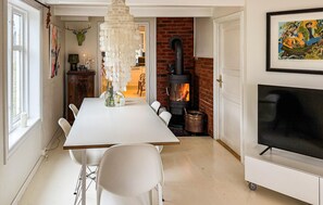 Un espace repas comprenant une table blanche, des chaises, un lustre, une cheminée et un téléviseur.