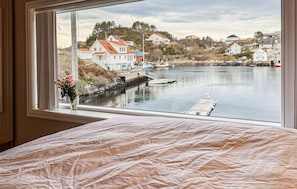 Une chambre avec une grande fenêtre donnant sur un plan d’eau paisible, une jetée et des maisons en arrière-plan.