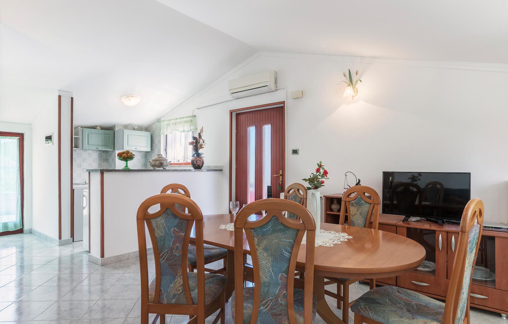 A dining area with a round table, wooden chairs, and a television on a wooden stand.