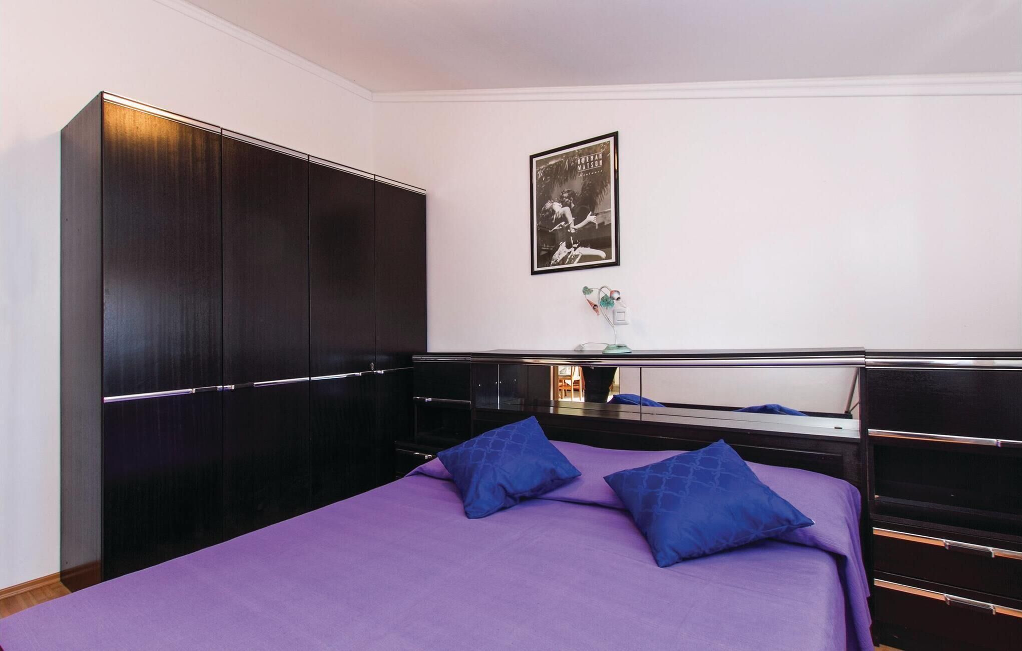 Una camera da letto con un ampio guardaroba, un letto con biancheria viola e un quadro incorniciato appeso al muro.