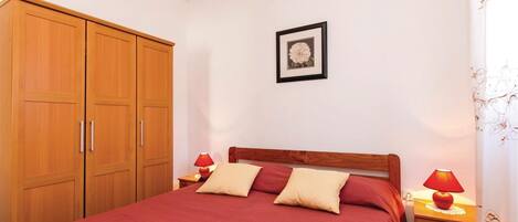 A bedroom with a bed, wooden wardrobe, two bedside lamps, and a framed picture on the wall.