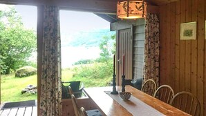 A wooden dining table with a white placemat, a bowl, and a candle holder. There are four chairs around the table. The room has wooden walls and a window with curtains. - Gorgeous home in Olden with house a mountain view (Olden)