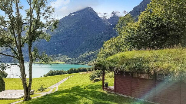 A mountain landscape with a lake, a path, and a red building with a thatched roof. - Gorgeous home in Olden with house a mountain view (Olden)