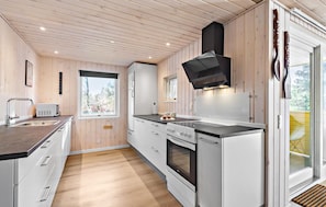 Eine moderne Küche mit Holzwandverkleidung, einem Edelstahl-Spülbecken, einem Einbauofen und einer schwarzen Dunstabzugshaube.