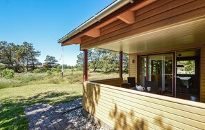 Eine Holzhütte mit überdachter Veranda, einem Essbereich mit Tisch und Stühlen sowie Blick auf den umliegenden Wald.