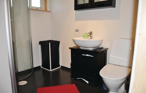 Et lille badeværelse med et hvidt toilet, et sort skab med en hvid vask og en rød måtte på gulvet.