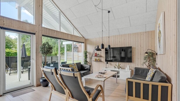 A spacious living room with a large TV, wooden flooring, and a balcony with outdoor furniture. - Gorgeous home in Sydals with sauna (Sydals)