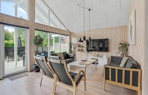 A spacious living room with a large TV, wooden flooring, and a balcony with outdoor furniture. - Gorgeous home in Sydals with sauna (Sydals)
