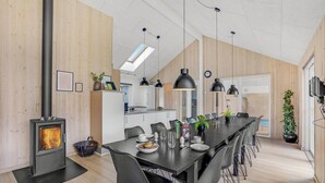 A modern kitchen with a wood stove, a dining area with a long table and chairs, and a kitchen counter. - Gorgeous home in Sydals with sauna (Sydals)