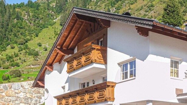 A white building with wooden balconies and a stone wall. - Ferienwohnung in Ischgl (Ischgl)