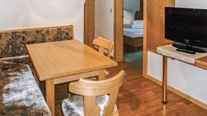 A small room with a wooden table and bench, a television on a stand, and a bed in the background. - Ferienwohnung in Ischgl (Ischgl)