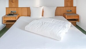 A neatly made bed with white linens and pillows, flanked by wooden nightstands with a small lamp and a charging device. - Ferienwohnung in Ischgl (Ischgl)