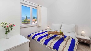 A bedroom with a bed, a bedside table, a nightstand, a window with a view, and a vase of flowers. - Holiday apartment with air conditioning and pool (����ilo)