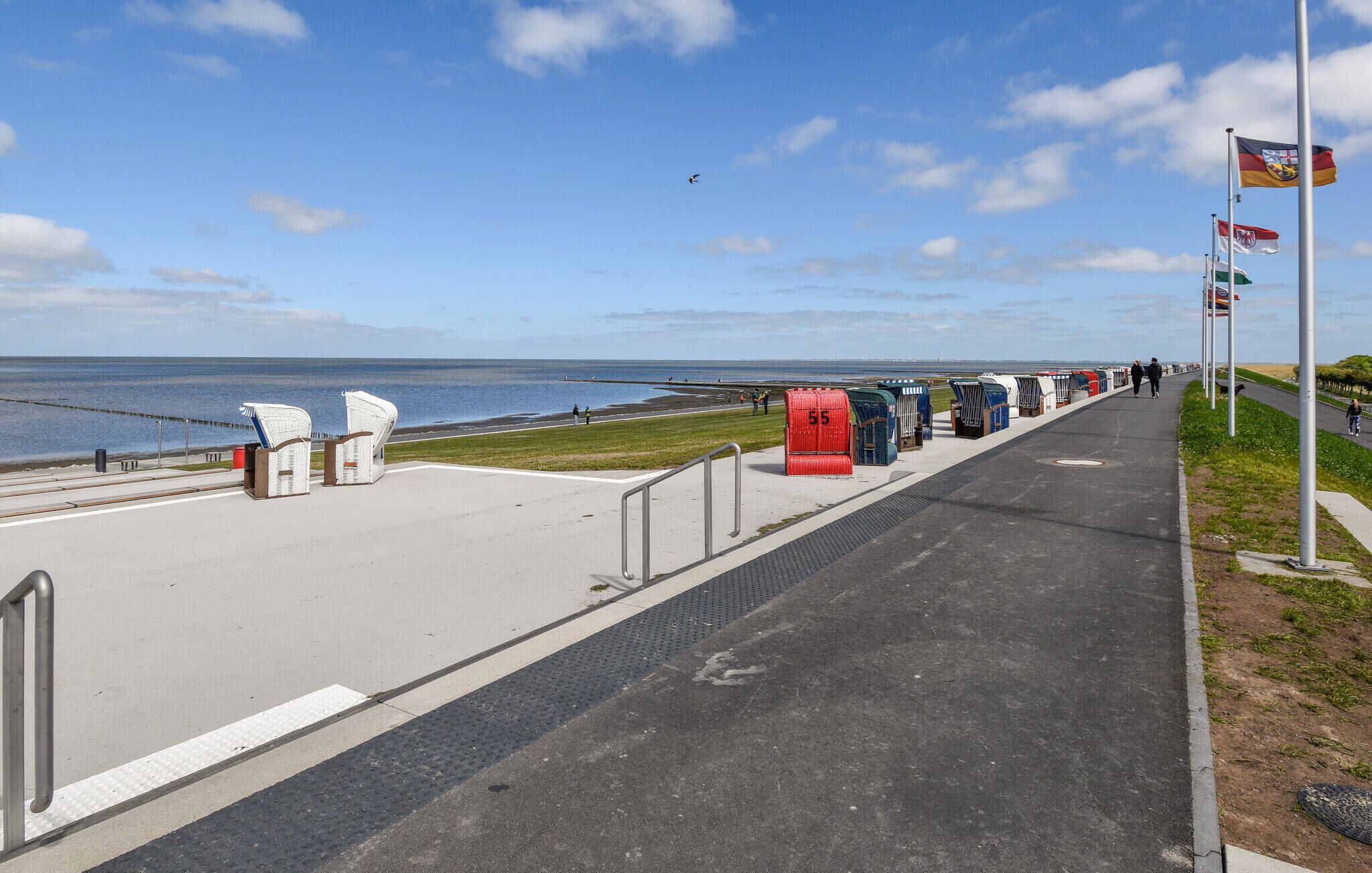 Eine Uferpromenade mit Bänken, einem Mülleimer und Flaggen.