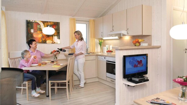 Une cuisine moderne avec des meubles en bois, un coin repas comprenant une table et des chaises, et un téléviseur fixé au mur.