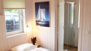 Une chambre à coucher avec un lit, une fenêtre donnant sur une voiture garée, une douche et un tableau représentant un voilier accroché au mur.