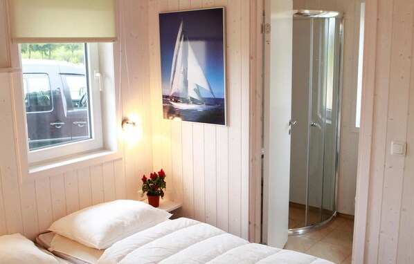 A bedroom with a bed, a window with a view of a parked car, a shower, and a sailboat painting on the wall.