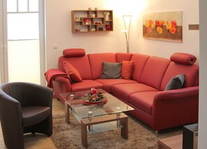 A living room with a red sofa, a glass coffee table, a dark armchair, and a wooden shelf with decorative items. - Meeresbrise Fireplace · Patio · 250 m to the beach - Meeresbrise Accommodation (Börgerende-Rethwisch)