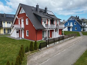 Une maison rouge avec un balcon, une maison bleue et une maison jaune, alignées les unes à côté des autres.